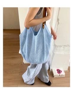 Detail of light blue knit tote bag with brown leather straps and gold metal rivets