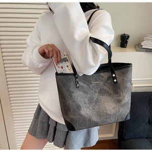 Detail view of large grey stone-wash tote bag with black leather handles on shoulder