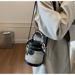 Detail of color-block bucket bag with silk scarf handle and leather stitching texture