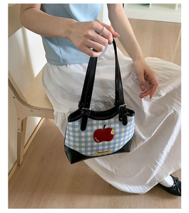 Close-up of blue plaid underarm bag with red apple embroidery and black leather straps