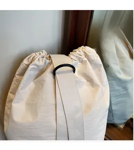Detail of beige canvas drawstring bag featuring wide shoulder straps and matte black rings