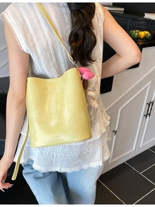 Minimalist pale yellow leather bucket bag with SNML logo and floral pendant on shoulder
