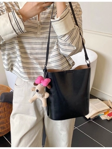 Minimalist black leather bucket bag with a plush dog charm shown on a female model