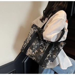 Detail of large black tote bag with silver bamboo leaf print worn by model on stairs