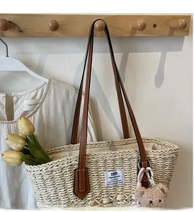 Dettaglio borsa tote in paglia intrecciata con spalline in pelle e ciondolo