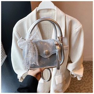 Detail of silver square bag featuring a large lace bow and shiny metallic ring handle