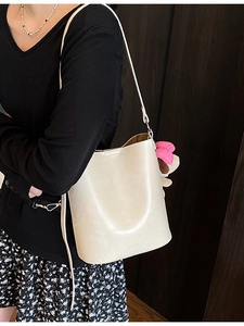 Chic cream-white bucket bag with a pink flower charm on a dark wooden background