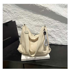 Détail du sac hobo en toile beige avec bandoulière réglable et pendentif tissé déco