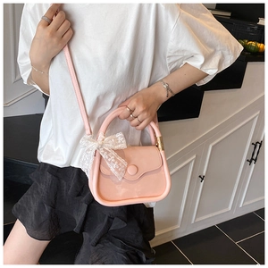Detailed shot of pink handbag featuring a white lace bow and round decorative buckle