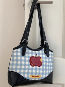 Blue and white plaid tote bag with apple patch and black leather straps on white door
