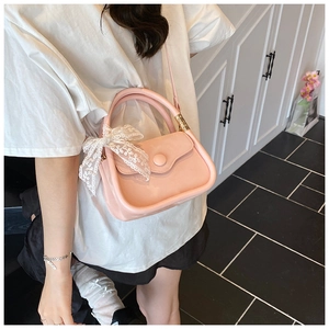 Detail of pink leather handbag with white lace bow and detachable strap on a model
