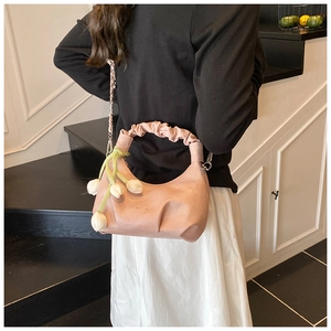 Detail of pink dumpling bag featuring pleated handle, metal chain, and tulip floral charm