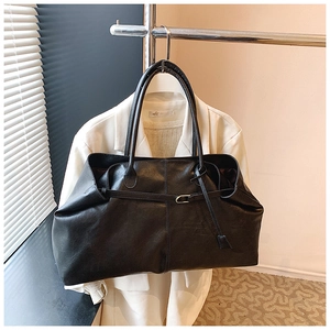 Detail view of large black leather tote bag with thin decorative strap and buckle
