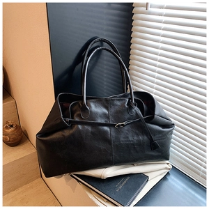 Close-up of soft black leather tote bag featuring decorative strap and long handles