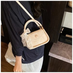Detail of cream crossbody bag with lace bow accessory worn on a navy and white outfit