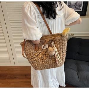 Dettaglio borsa tote in paglia con tracolla in pelle e ciondolo a forma di orso