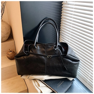 Detail of a black leather tote bag featuring a vintage texture and a slim buckle accent