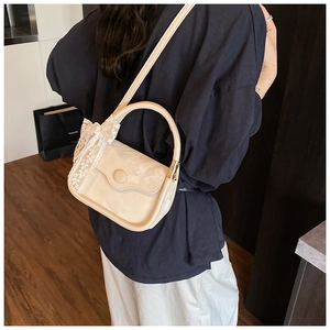 Detail of cream crossbody bag with glossy patent finish and white lace bow decoration
