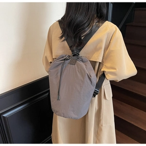 Detail of grey drawstring bucket bag with adjustable strap worn by a model in a trench coat
