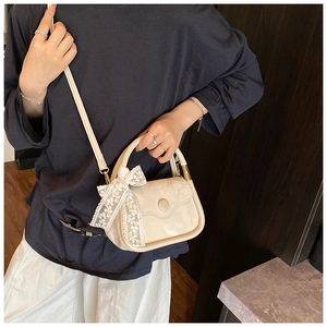 Detailed view of beige crossbody bag featuring white lace bow and round buckle accents