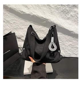 Gros plan d'un sac bandoulière noir avec un pendentif décoratif en anneau blanc