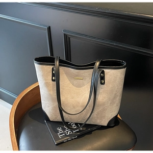Detail of taupe textured tote bag with black trim and gold hardware on a vintage chair