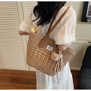 Dettaglio di borsa tote in paglia con manici in pelle marrone e ciondolo a forma di orso