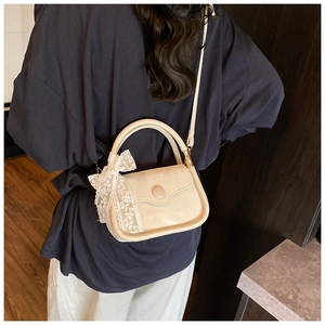 Detail of a beige PU leather crossbody bag featuring a white lace bow and round clasp