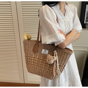 Dettaglio di una borsa tote in paglia intrecciata con manici in pelle e ciondolo a orsetto
