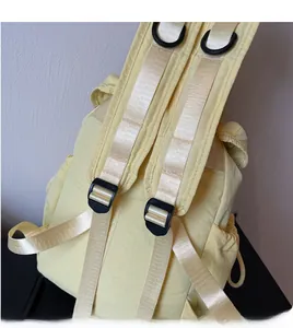 Detail of adjustable nylon straps and black D-rings on a light yellow backpack
