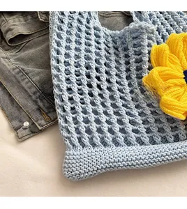 Detail of light blue knit tote bag showing intricate crochet weave and yellow 3D flower