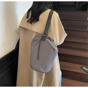 Detailed view of a grey drawstring nylon shoulder bag styled with a khaki trench coat