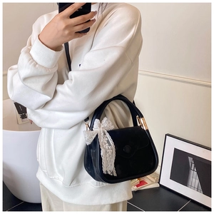 Detail of black suede handbag featuring gold buckle and white lace bow accessory