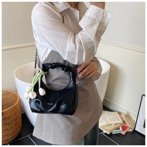 Detail of black pleated handbag with metal chain strap and white floral charm
