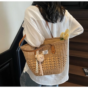 Dettaglio di borsa tote in paglia intrecciata con manici in pelle e ciondolo a orsetto