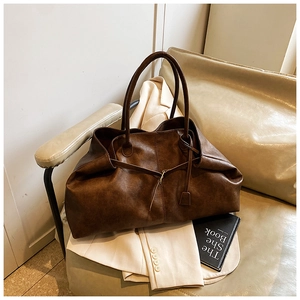 Detail of a large dark brown tote bag on a beige sofa with a vintage relaxed style