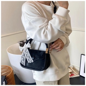 Detail of black leather handbag with white lace bow and gold metal hardware accents