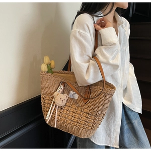 Dettaglio borsa tote in paglia con manici in pelle marrone e ciondolo a forma di orso
