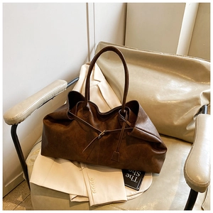 Detail of a large dark brown retro tote bag with matte faux leather texture on a leather chair