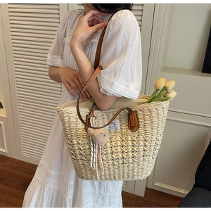 Dettaglio borsa tote in paglia intrecciata con manici in pelle marrone e pon pon decorativi