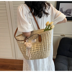 Dettaglio borsa tote in paglia intrecciata con manici in pelle marrone e portachiavi orsetto