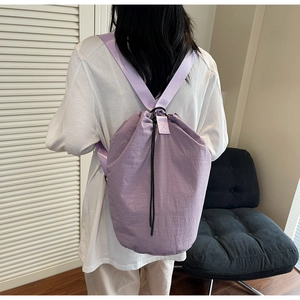 Rear view of a casual purple drawstring bucket bag worn by a model in a cozy interior