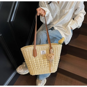 Dettaglio di borsa tote in paglia con manici in pelle marrone e ciondolo a forma di orso