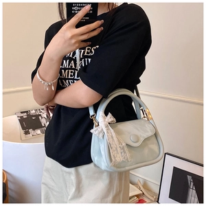 Detail of light blue crossbody bag with glossy finish and large white lace bow