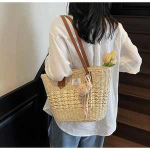 Dettaglio borsa tote in paglia intrecciata con manici in pelle e pendente orso