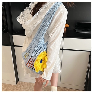 Detail of light blue crochet mesh bag featuring a large yellow knitted 3D flower accent