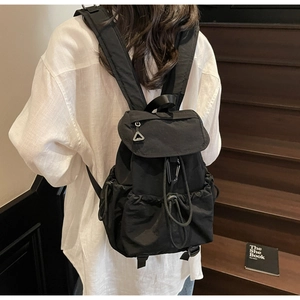 Classic black nylon drawstring backpack with flap cover shown on model in cozy indoor setting