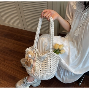 Detailed knit texture of white woven tote bag with a brown plush bear pendant