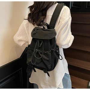 Detail of black nylon drawstring backpack with flap closure shown on model's back