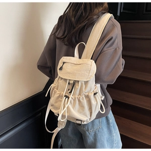 Beige nylon drawstring backpack with flap closure shown on a model in a casual setting